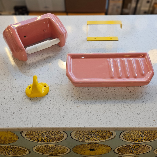Roze en gele wcrolhouders, zeepbakje en geel kledinghaakje van porselein op natuurstenen ondergrond.